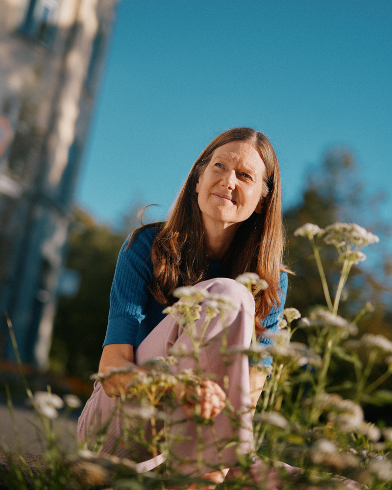 Foto av Sally O'Halloran sittende blant blomster, blå himmel.