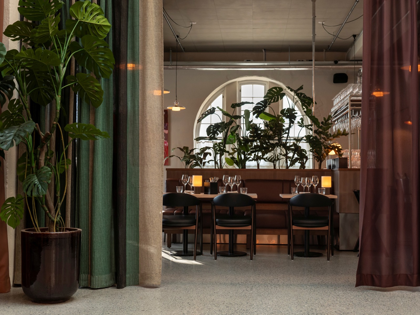Interiørfoto av restaurant, pådekt bord, grønne planter, rundt vindu, gardiner.