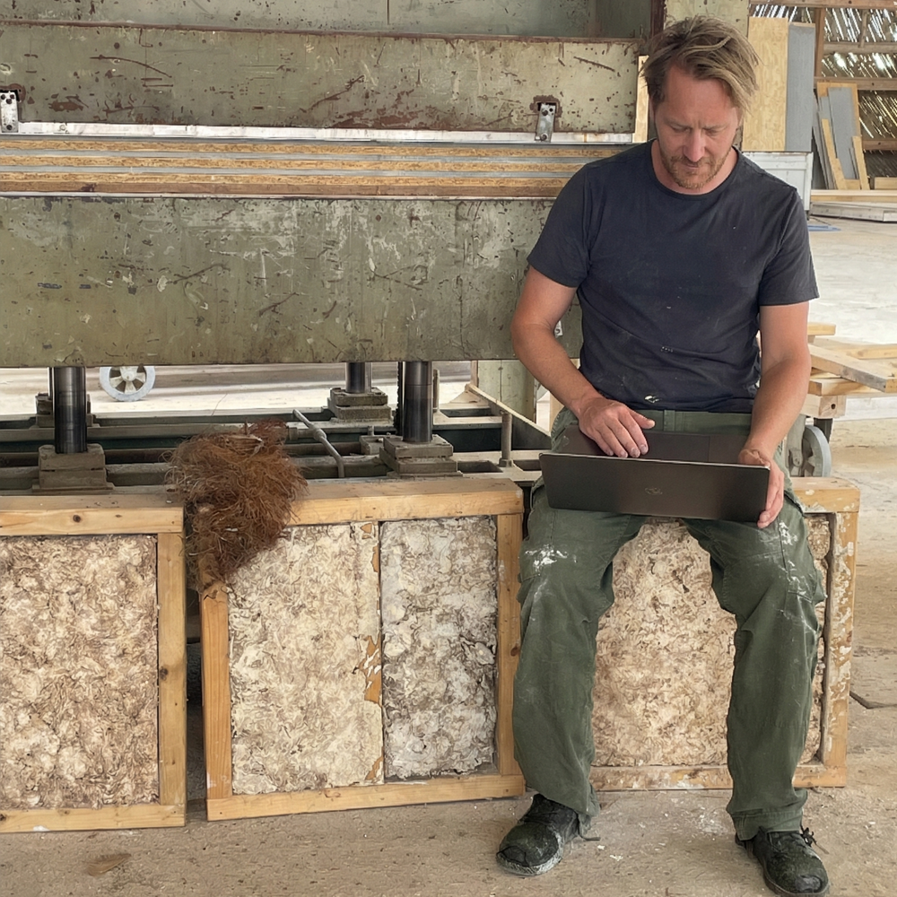 Foto av en mann som sitter på noen kasser med coco-crete og jobber på en pc.