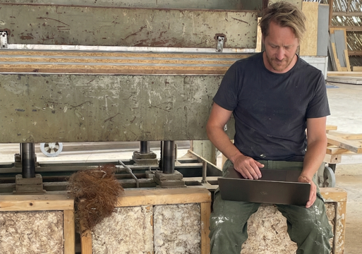 Foto av en mann som sitter på noen kasser med coco-crete og jobber på en pc.