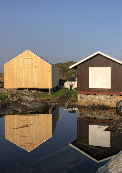 Foto av tre naust liggende langs vannkanten.