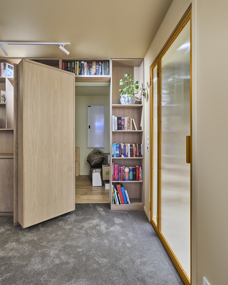 Interiørfoto som viser teknisk rom skjult av plassbygde bokhyller og dør i tre