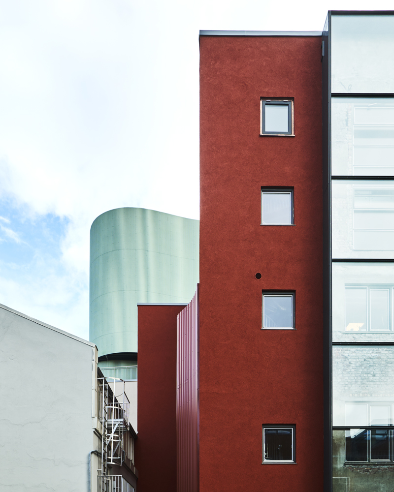 Eksteriør foto av en rød fasade med glassfelt og organisk grønn form i bakgrunnen.