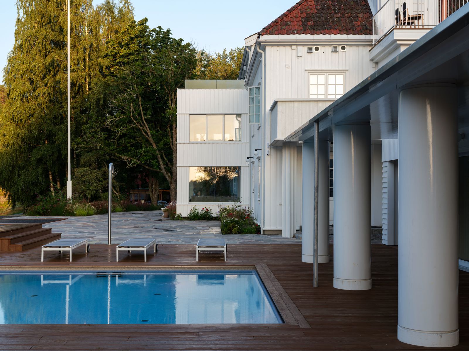 Foto av resort med hvitmalt bygg, store søyler, badebasseng og trær i bakgrunnen.