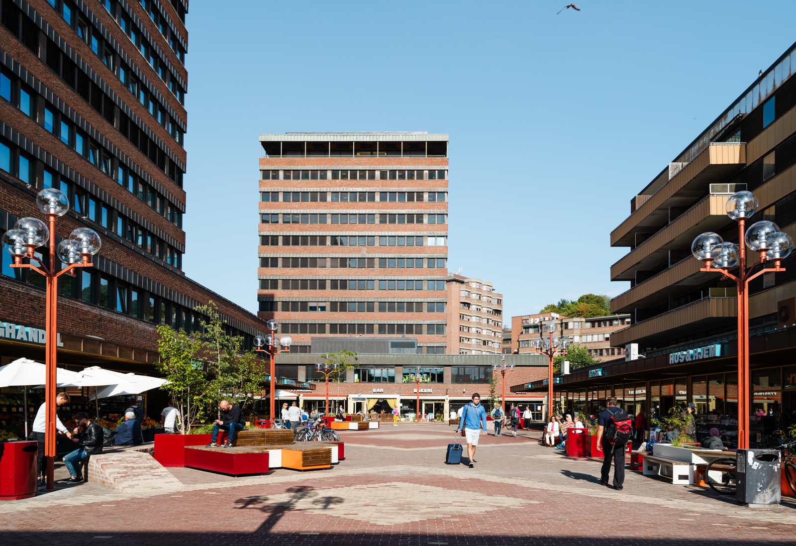 Tøyen Torg med ulike sitte elementer, mennesker og teglbygg som omkranser plassen. Foto.