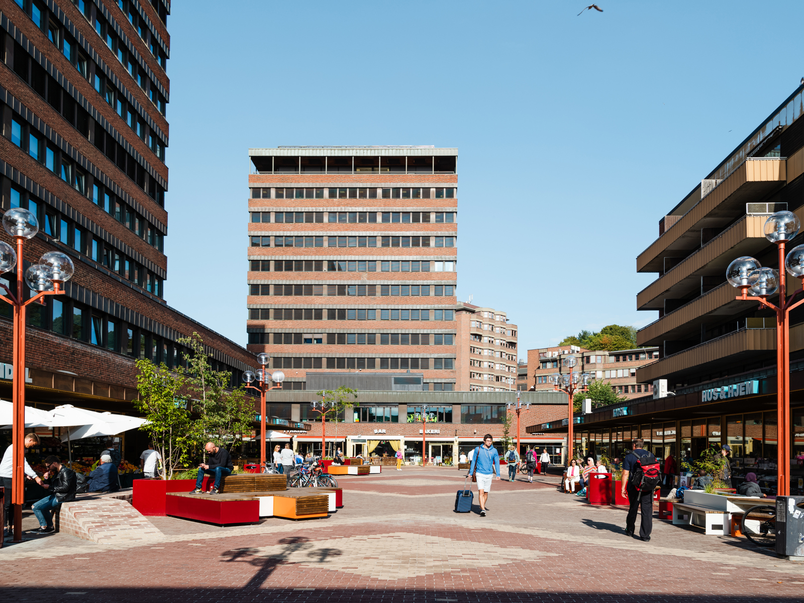 Tøyen Torg med ulike sitte elementer, mennesker og teglbygg som omkranser plassen. Foto.