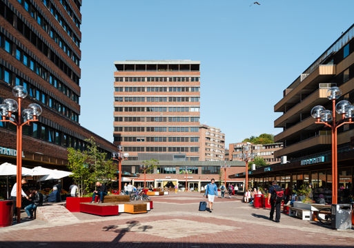 Tøyen Torg med ulike sitte elementer, mennesker og teglbygg som omkranser plassen. Foto.