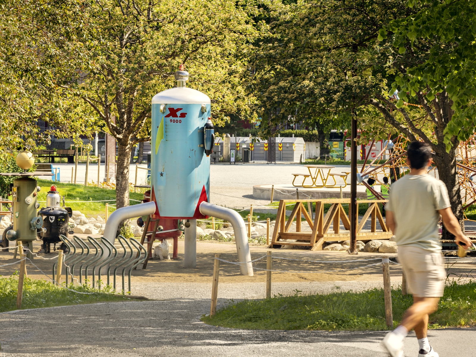 Foto av Buranbanen aktivitetspark med mange ulike fargerike skulpturer, en mann som går på en grus sti fremst i bildet. 