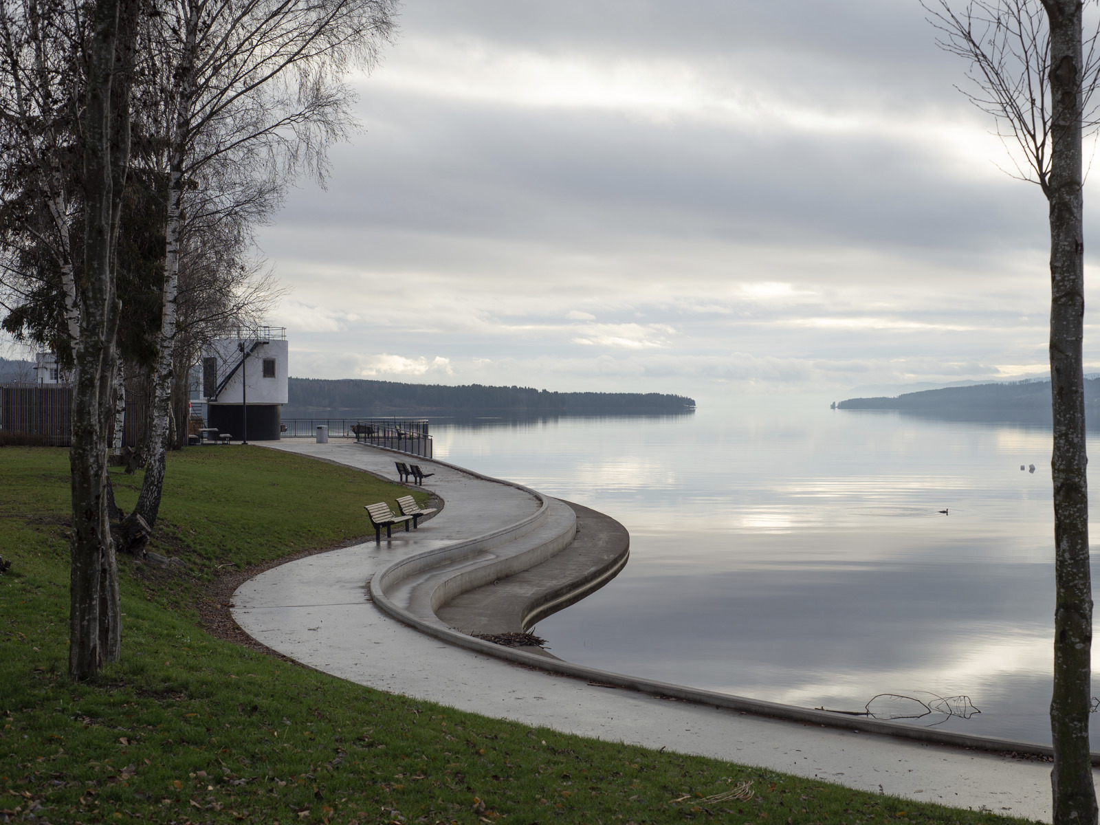 Foto av kurvet vannkant med amfi, plen og benker.