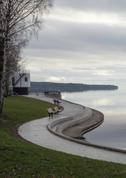 Foto av kurvet vannkant med amfi, plen og benker.