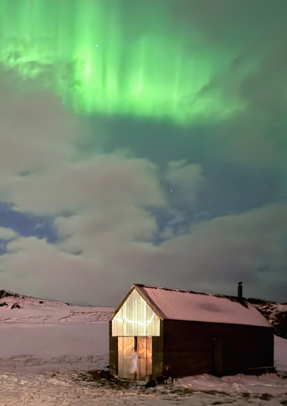 Foto av badstue som er opplyst innenfra  i snølandskap med nordlys over.