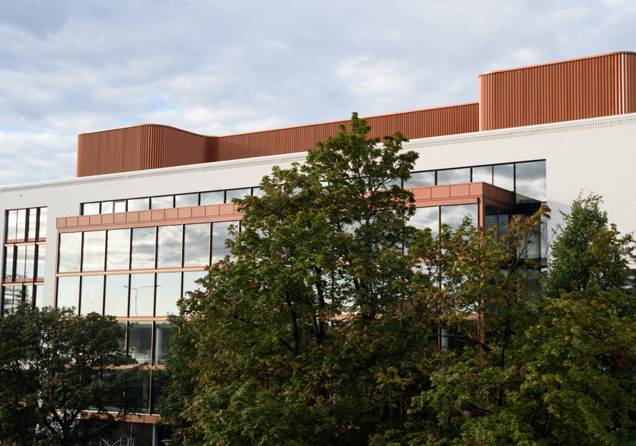 Fasadefoto av kommunegården i Sandvika, trær i forgrunn, bygg i hvit og oransje i bakgrunnen.
