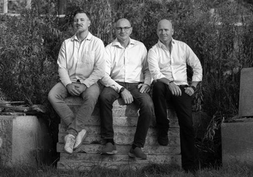 Foto av tre menn i skjorte som sitter på steinheller. 