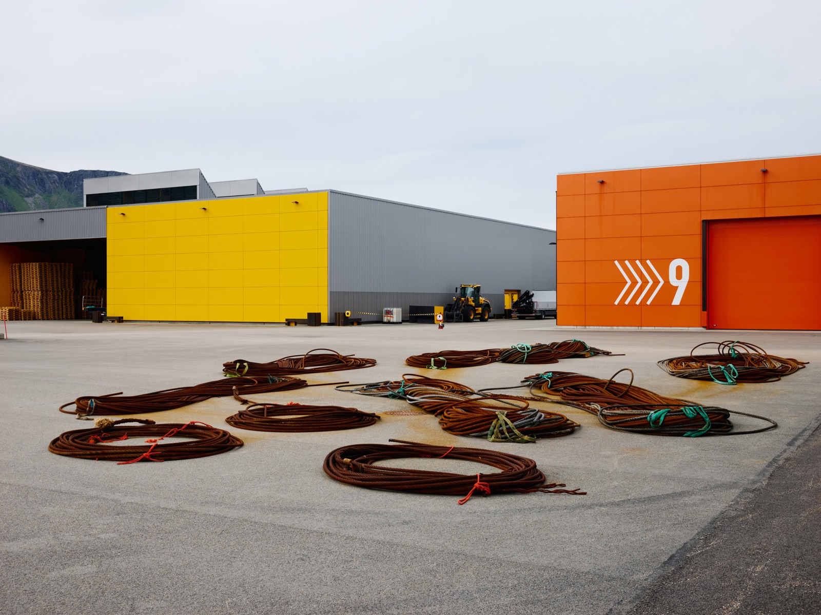 Eksteriørfoto over anlegget til Holmøy Maritime. To bygg vises, et i gult og det andre i orange, med kabler liggende på bakken foran