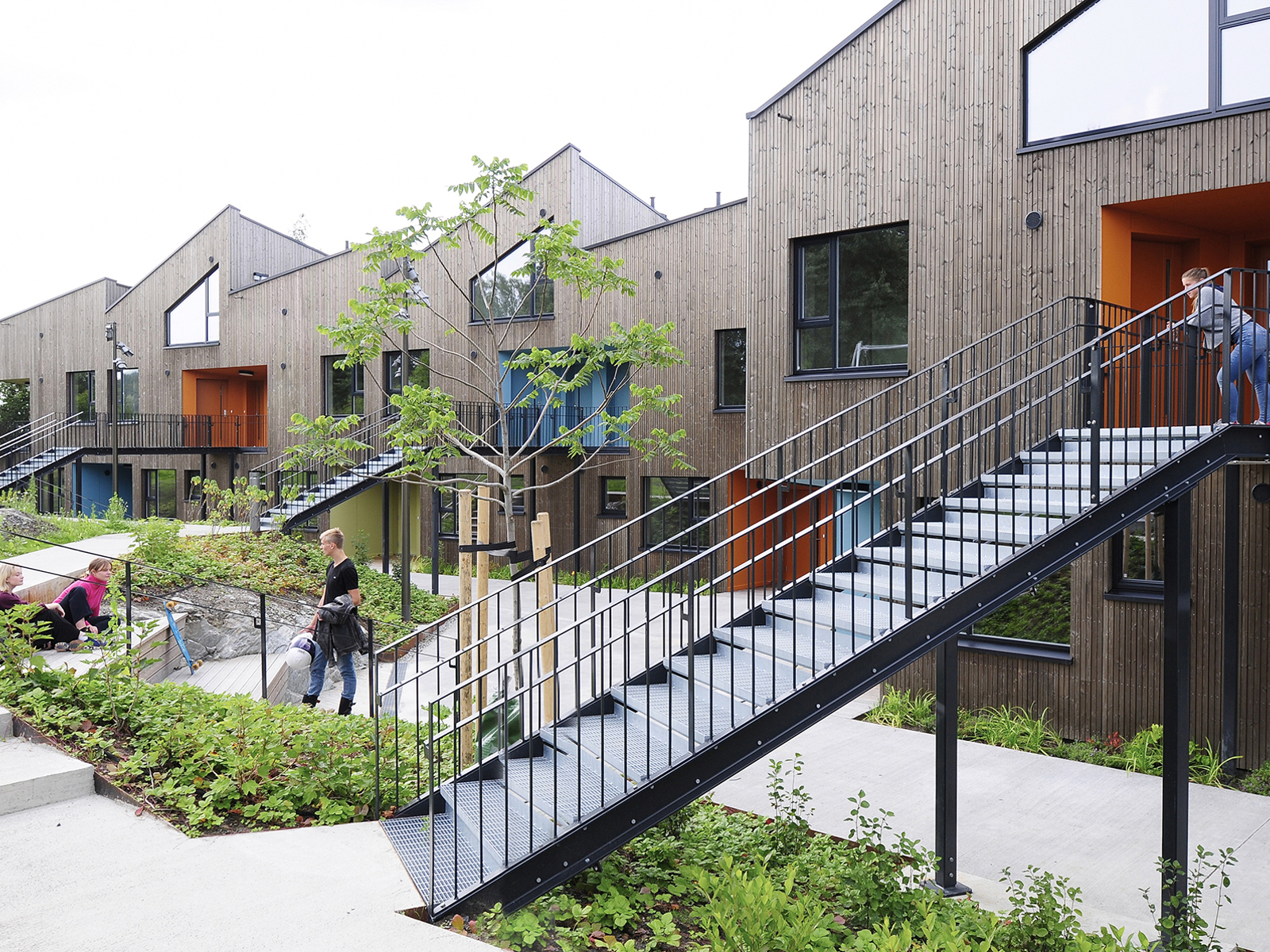 Rekkehus med svarte trapper ned fra 2.etg. folk som oppholder seg utenfor i det grønne. Foto.