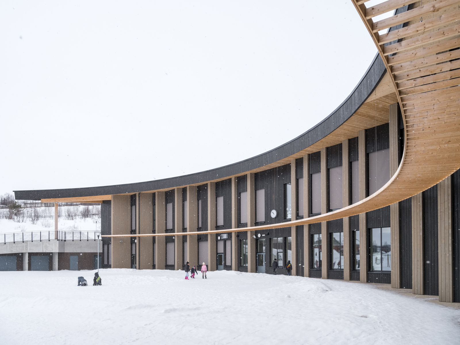 Foto av snøkledd skolegård omringet av kurvet skolebygg. 