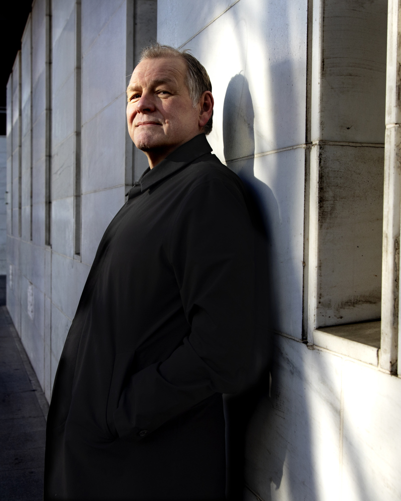 Portrett av Atle Aas lent inntil en vegg ute. Foto.