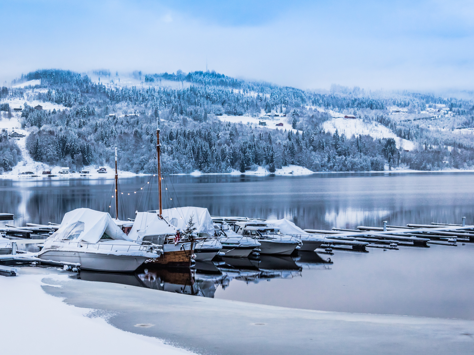 Vinter foto av vann og fjell med snø, båter ligger langs brygge.