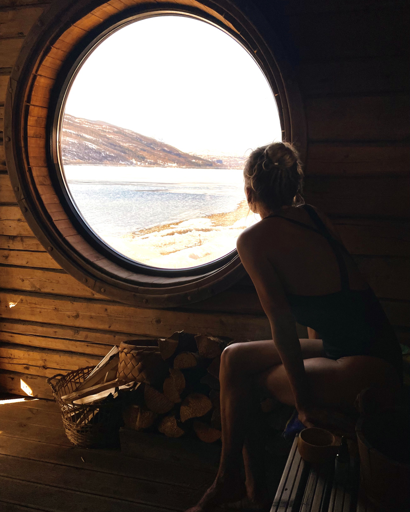 Interiør foto av en dame som kikker ut av et rundt vindu i en sauna. 