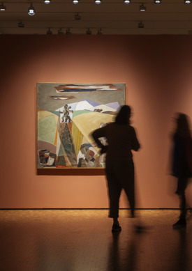 Uklare silhuetter av mennesker som står fremfor et bilde hengende på en oransje vegg i et utstillingsrom. Foto.