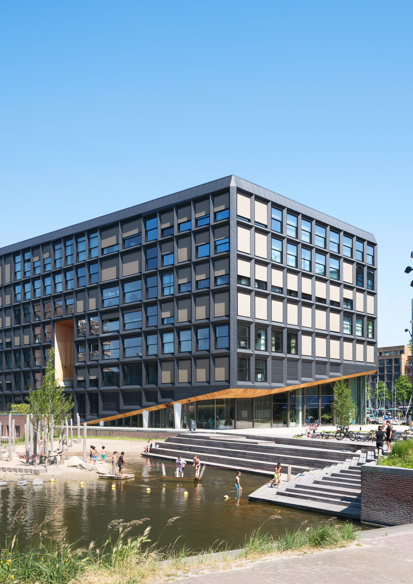 Foto av fasade på boligprosjekt, vann og uteområde i forgrunnen, barn som leker. 
