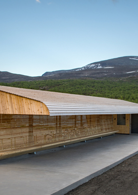 Reinsvangen servicebygg, Overbygg i treverk med integrerte sittebenker, runde former på tak. Fjell i bakgrunn. Foto.