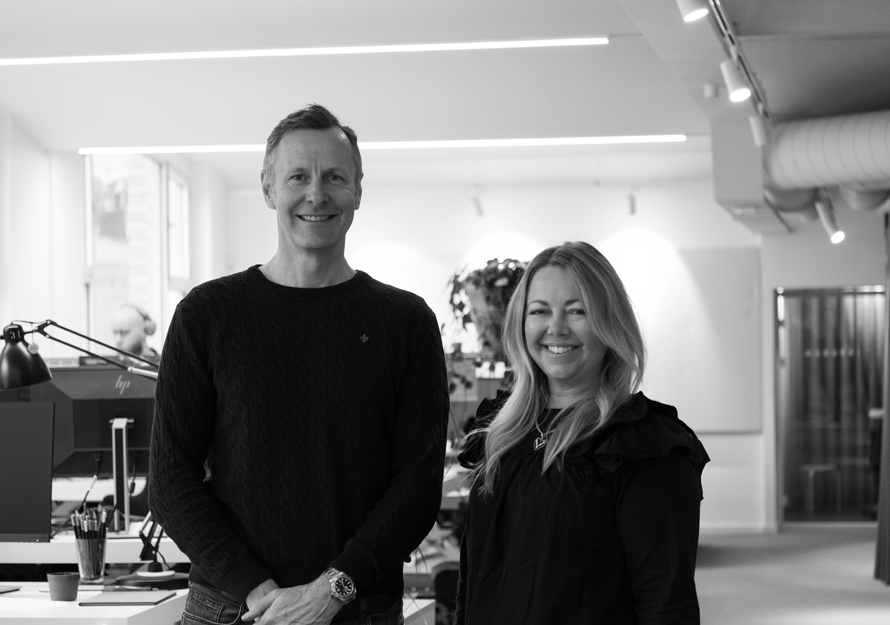 Sort-hvitt-foto av konsernsjef i Mad, Nicolai Riise og ny kommunikasjonssjef i Mad, Victoria Bryde, i et kontorlandskap.