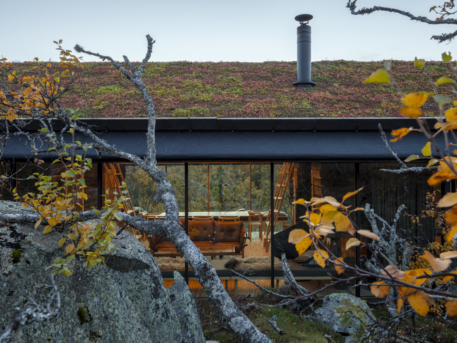 Foto av hytte i høstlandskap, stor stein i forgrunnen.