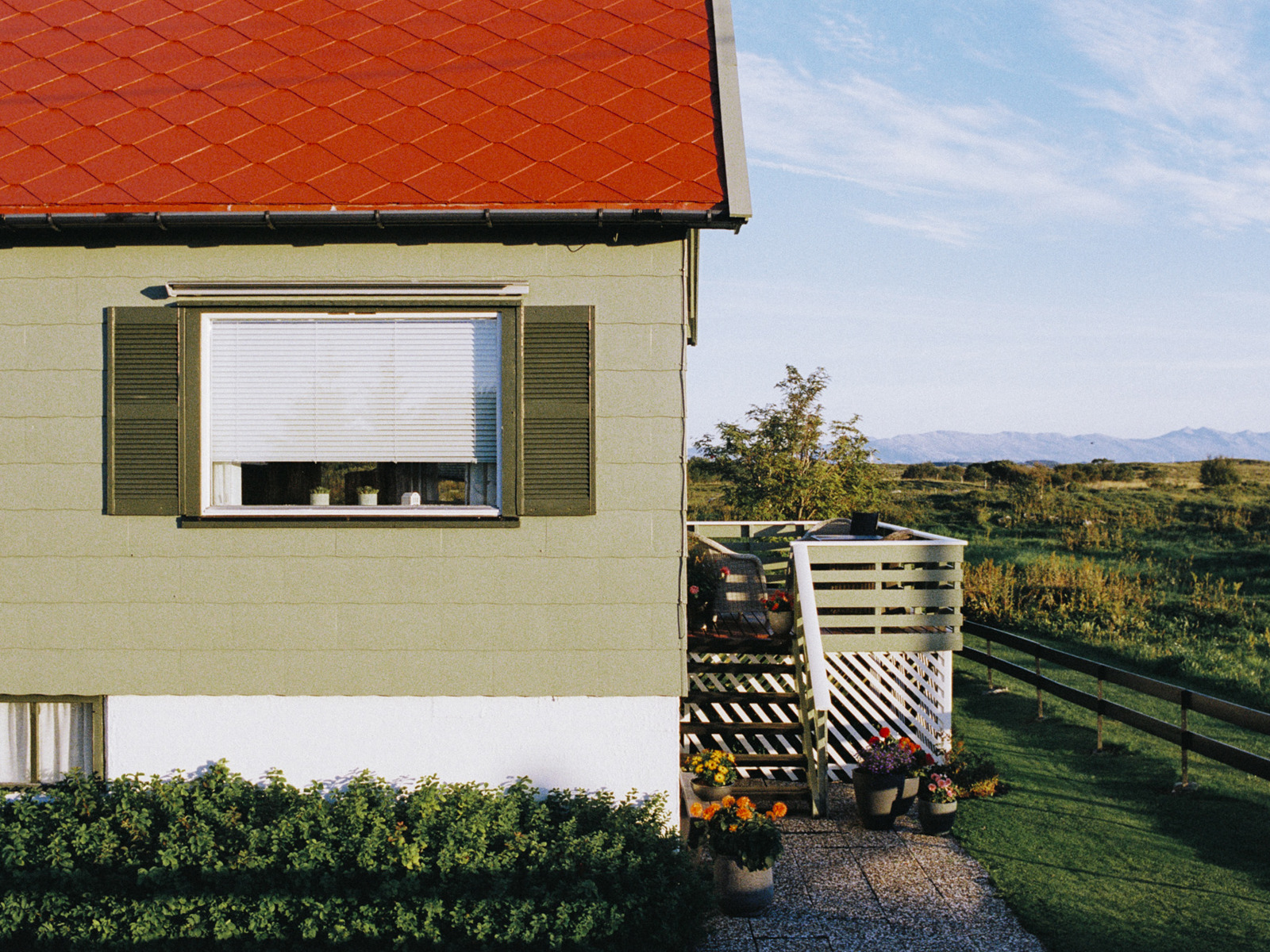 Foto av et hus med rødt tak og eternittplater på fasaden.