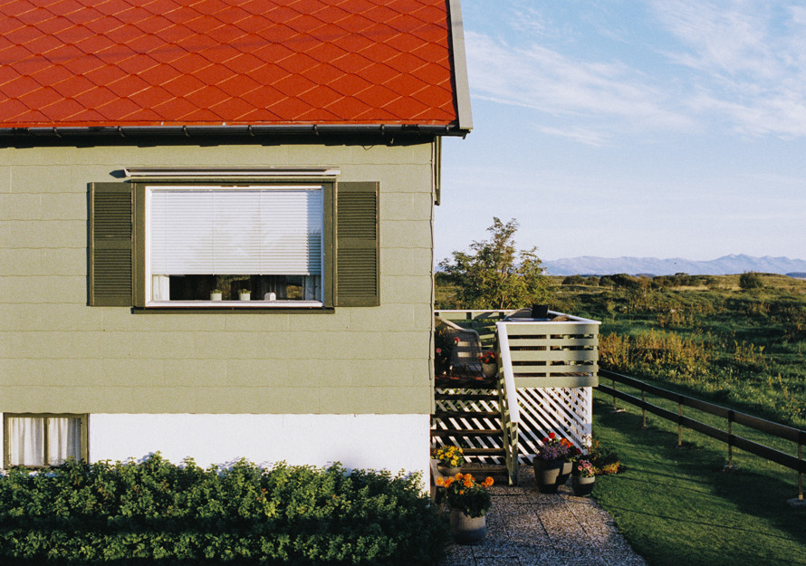 Foto av et hus med rødt tak og eternittplater på fasaden.