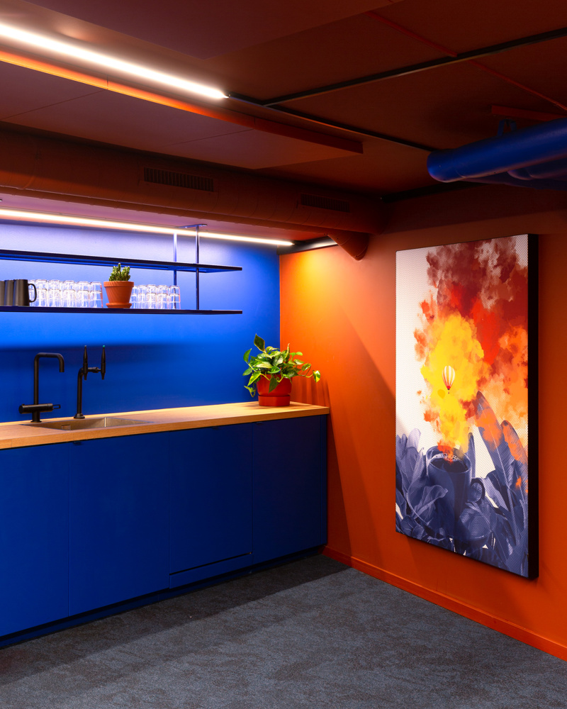 Kjøkkenhjørne i blå, maleri hengende på oransje vegg. Foto.
