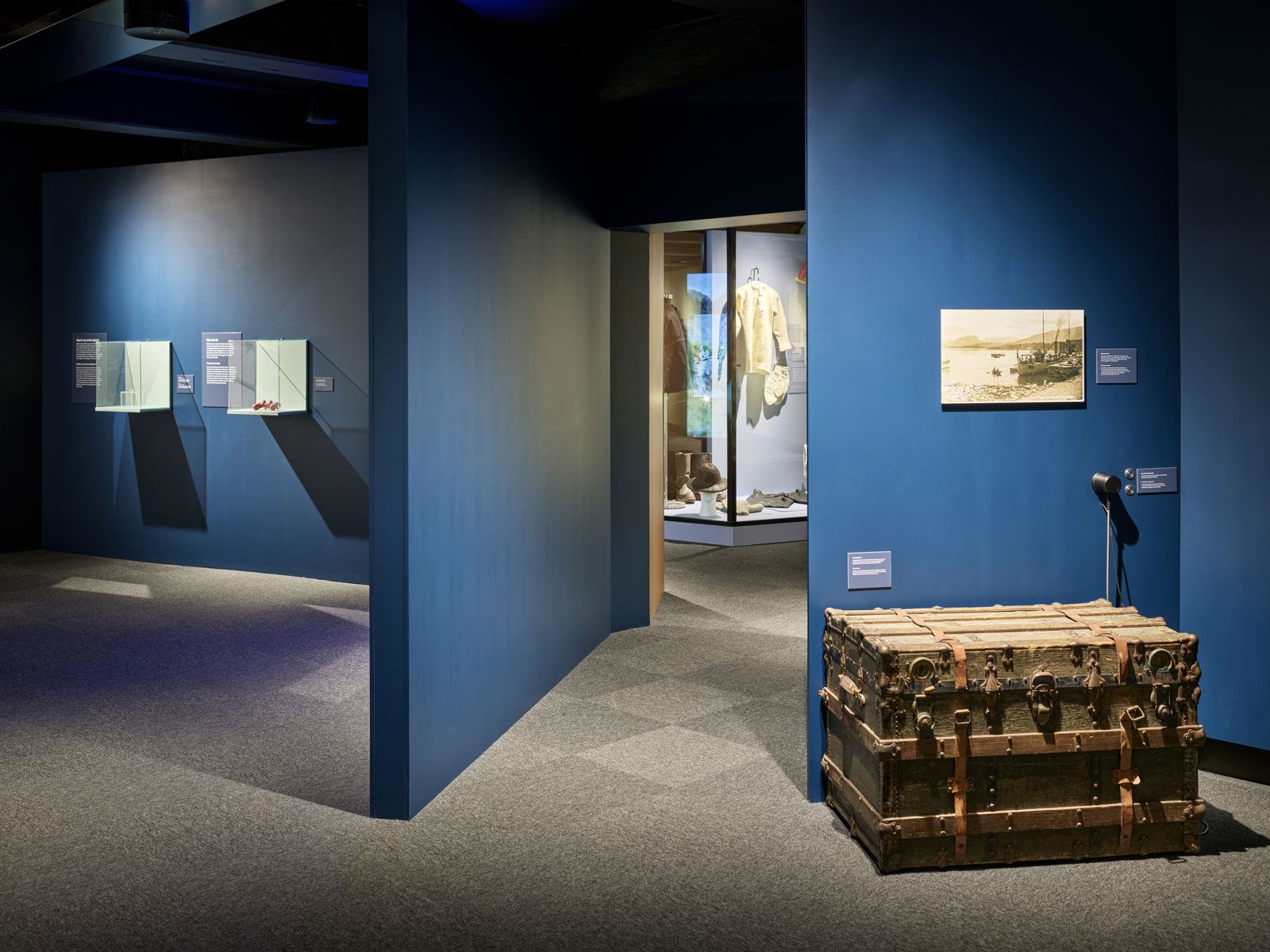 Utstillingsrom med blå vegger i ulike vinkler, en stor kiste og diverse andre ting er stilt ut. Foto.
