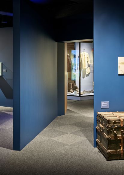 Utstillingsrom med blå vegger i ulike vinkler, en stor kiste og diverse andre ting er stilt ut. Foto.