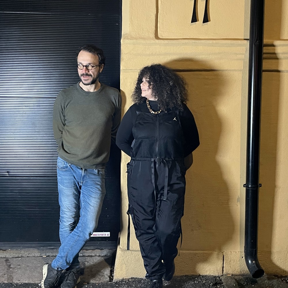 Dana Jdid og Nizam Najjar lener seg inntil en gul vegg. Foto.
