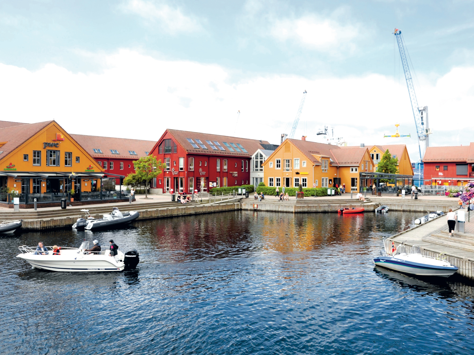 Havn, båter på vannet, fargerike hus med saltak på land. Foto.