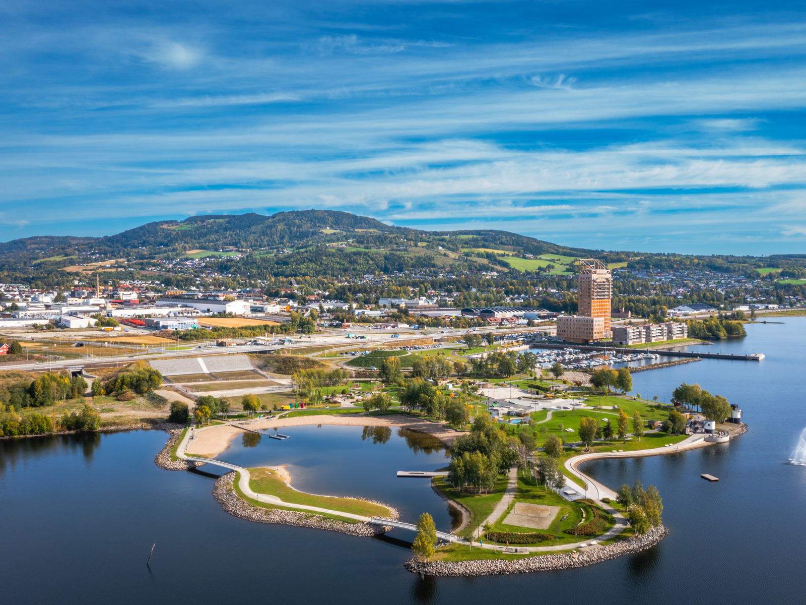 Fly/drone foto av parkområde som går ut i vannet, by i bakgrunnen. 