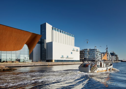 Foto av Kunstsiloen i Kristiansand i kontekst, vann og båt i forgrunnen.