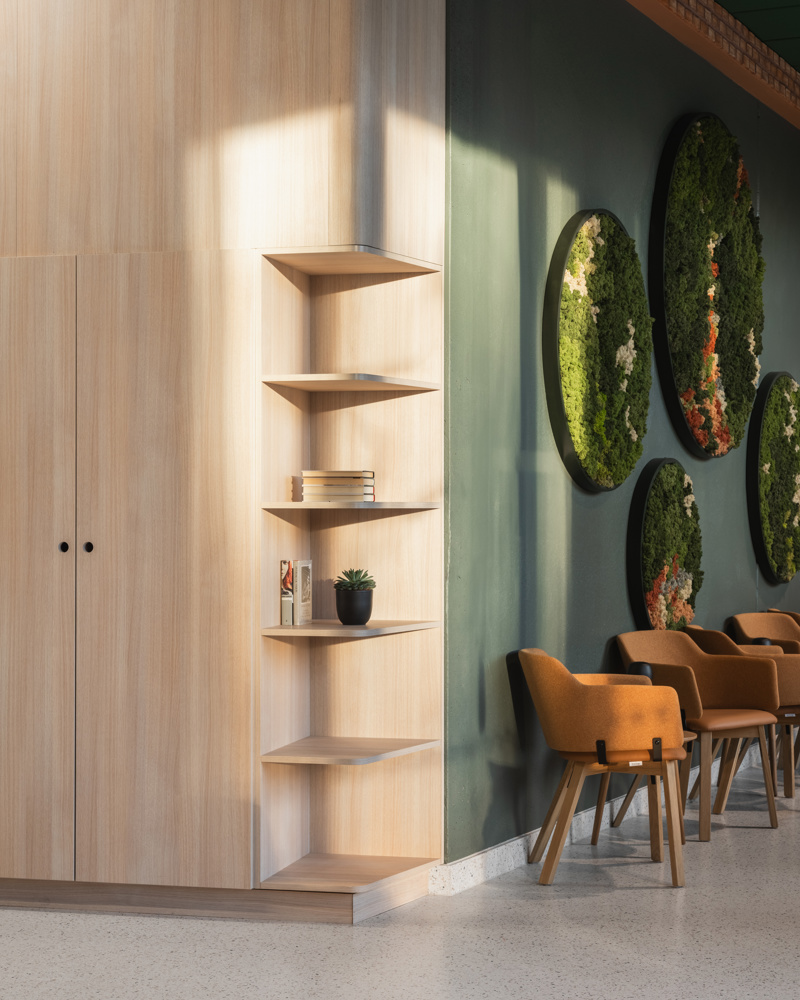 Interiør foto av et hjørne i treverk med innebygde hyller som møter en grønn vegg.