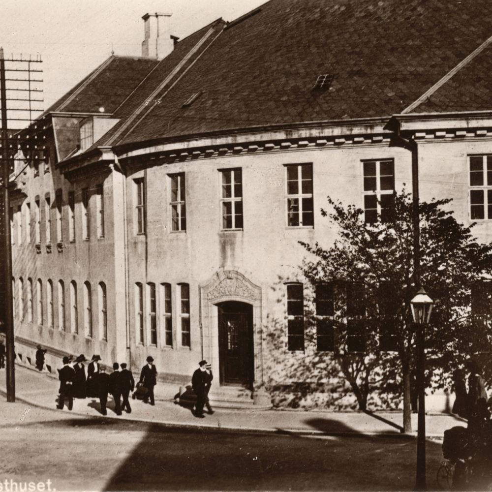 Bygg i et veikryss, mange mennesker i gata, sepia. Foto.