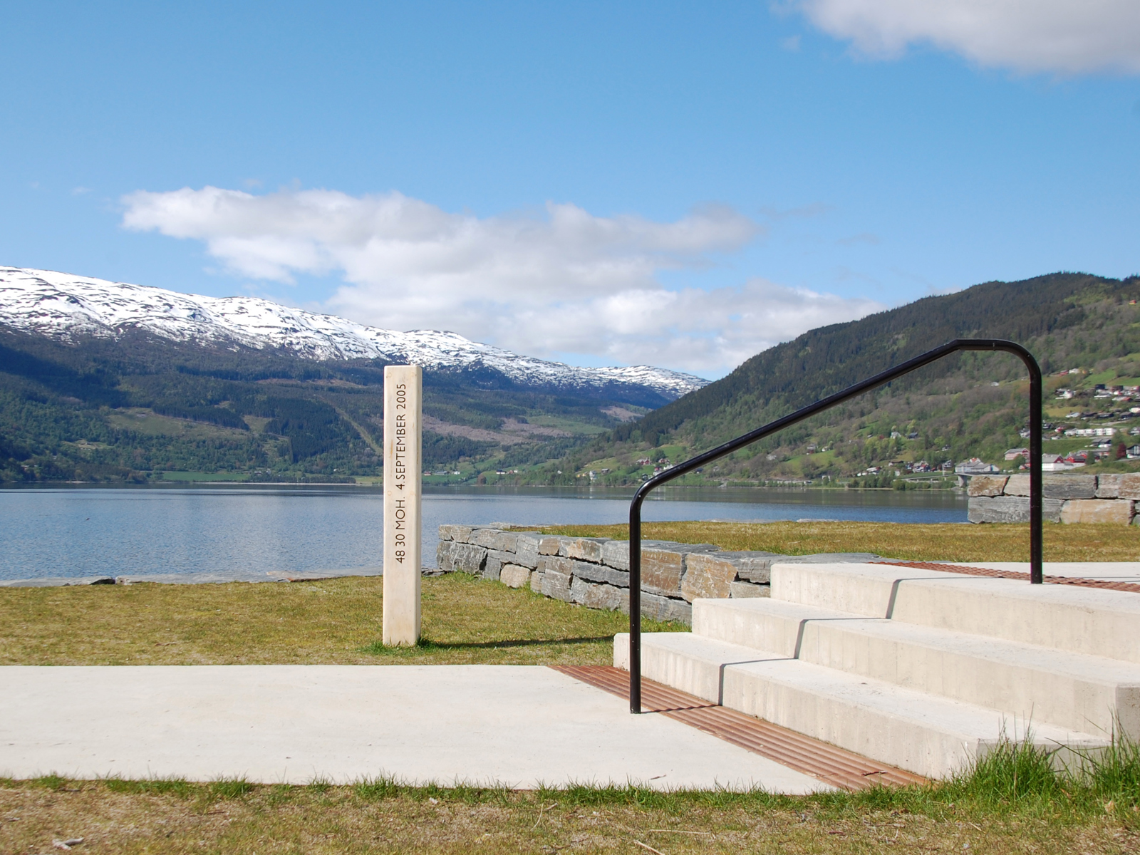 Foto av søyle som viser vannstand, trapp, vann og fjell i bakgrunnen.